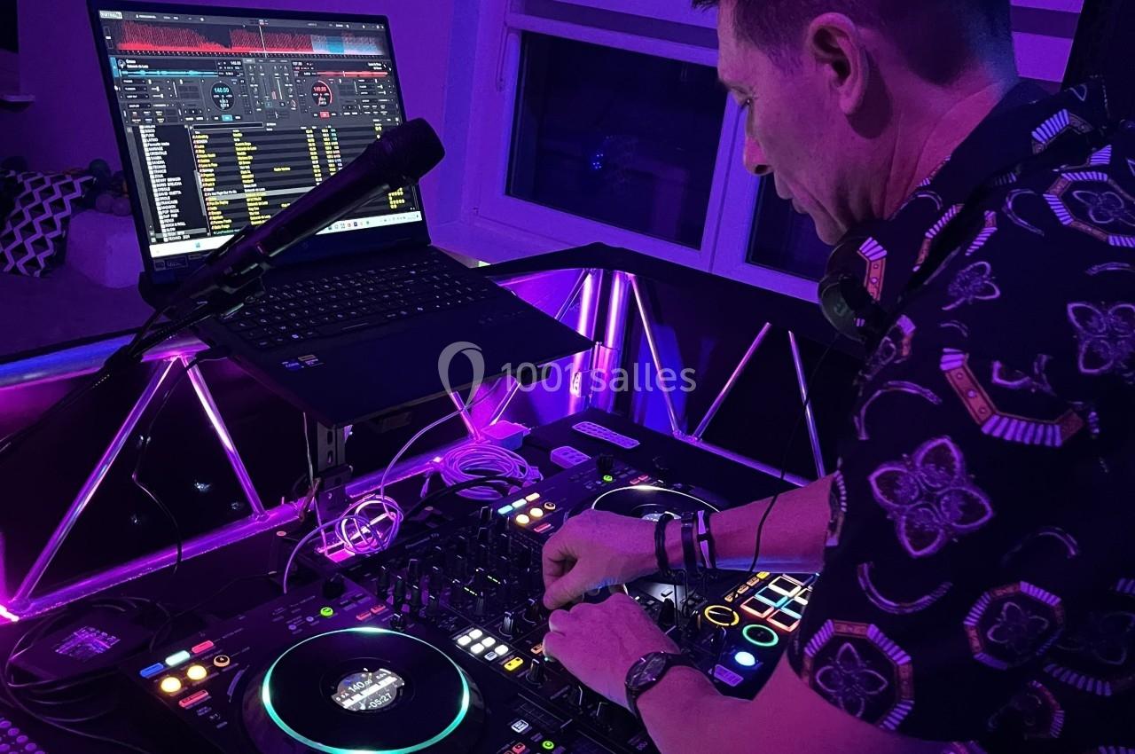 Un DJ mixe de la musique sur une console éclairée par des lumières violettes, avec un ordinateur portable ouvert.