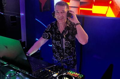 Un DJ mixe de la musique sur une table de mixage dans un environnement lumineux avec un écran affichant des visuels…