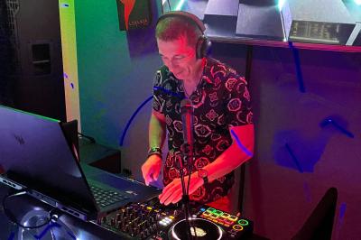 Un DJ mixe de la musique sur une table de mixage dans un environnement lumineux avec un écran affichant des visuels…