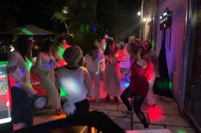 Des personnes dansent en soirée en extérieur, éclairées par des lumières colorées, dans une ambiance festive.