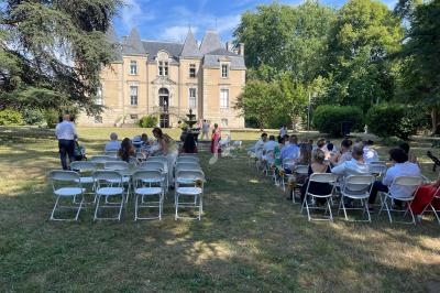 Des invités assis en plein air assistent à une cérémonie devant un château entouré d'arbres.