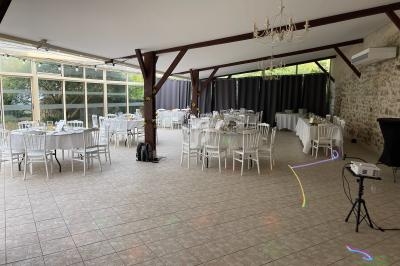 Salle de réception lumineuse avec tables rondes et chaises blanches, décorée pour un événement, avec un projecteur au…