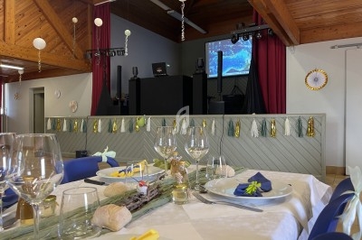 Salle décorée pour un événement avec tables dressées, décorations festives et une scène équipée d'un écran et de matériel…