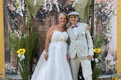 Un couple en tenue de mariage pose devant une décoration florale avec des tournesols et des guirlandes blanches.