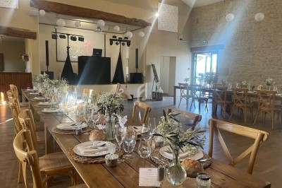 Salle de réception décorée avec des tables en bois, des chaises assorties et une scène équipée pour un événement festif.