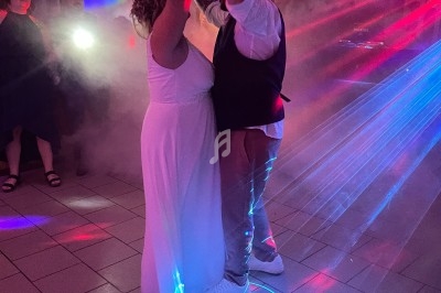 Un couple danse sous des lumières colorées et des effets de fumée dans une salle.