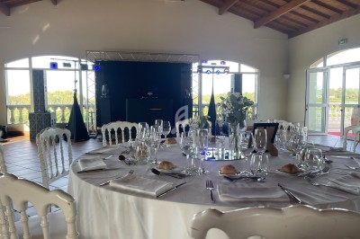 Salle de réception lumineuse avec tables dressées, nappes blanches, vaisselle élégante et vue sur l'extérieur verdoyant.