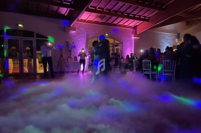 Un couple danse au milieu d'une piste enveloppée de fumée, entouré d'invités dans une salle éclairée de lumières colorées.
