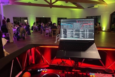 Poste de DJ avec ordinateur portable et platines en premier plan, salle éclairée avec invités assis en arrière-plan.