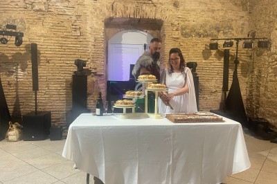 Un couple coupe un gâteau de mariage sur une table décorée, dans une salle aux murs en pierre.