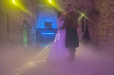 Un couple danse dans une salle en pierre éclairée de lumières colorées, entouré de fumée au sol.