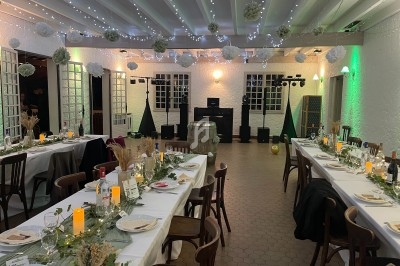 Salle décorée pour un événement avec tables dressées, guirlandes lumineuses au plafond et ambiance chaleureuse.