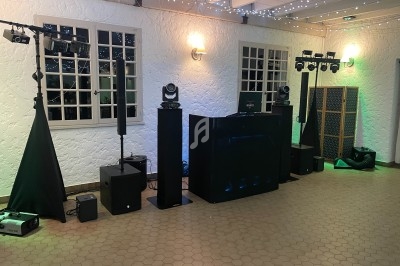 Installation de matériel de sonorisation et d'éclairage dans une salle avec murs blancs et guirlandes lumineuses.