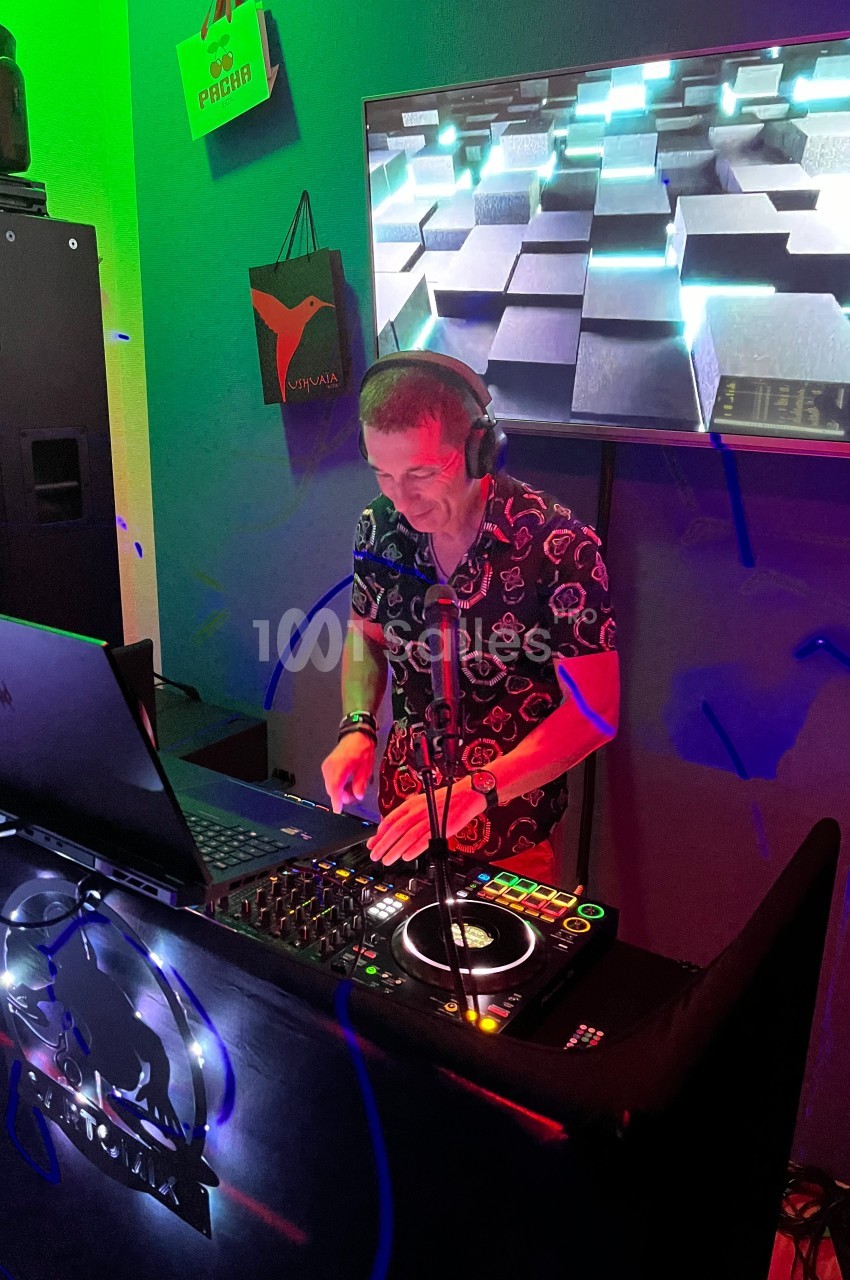 Un DJ mixe de la musique sur une console dans une ambiance lumineuse avec un écran affichant des visuels en arrière-plan.