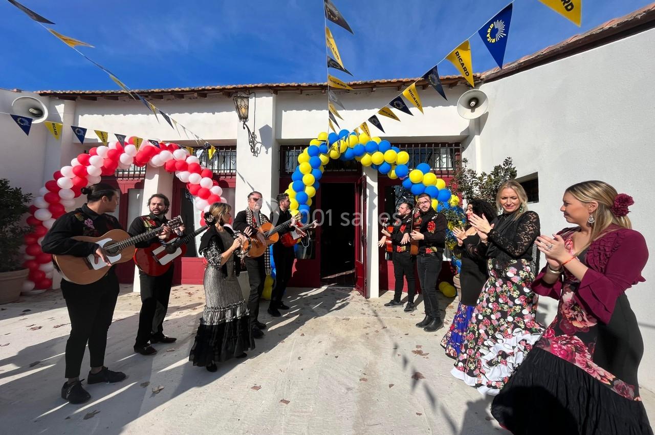 Des musiciens et danseurs en tenue traditionnelle se produisent devant un bâtiment décoré de ballons et de fanions.