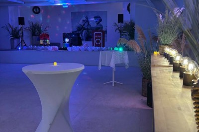 Tables élégamment dressées avec nappes blanches, serviettes pliées, verres et décorations florales dans une salle lumineuse.