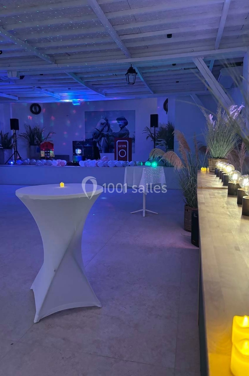 Salle décorée pour un événement, avec éclairage tamisé, bougies, tables hautes et plantes en arrière-plan.