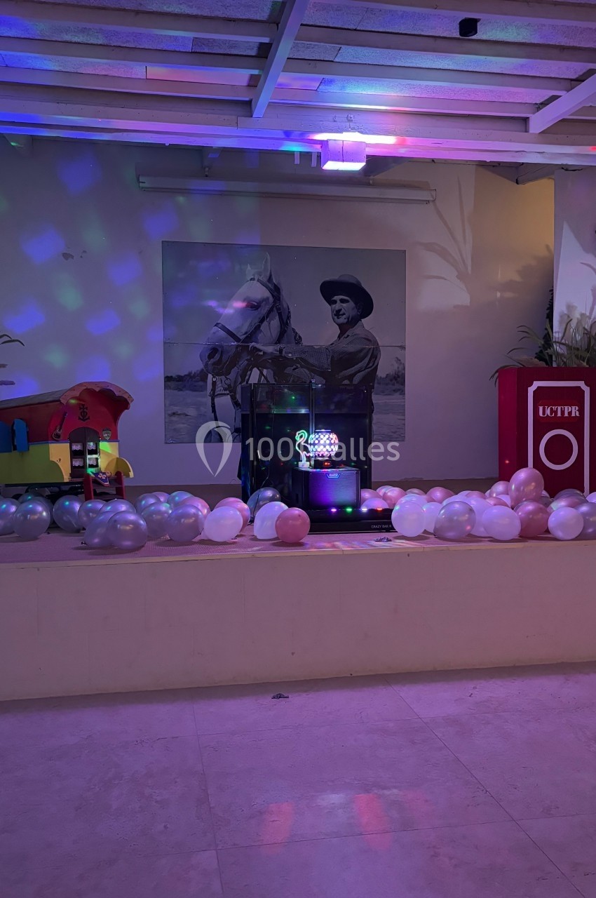 Scène décorée avec ballons colorés, éclairages festifs, et une photo en noir et blanc d'un homme à cheval en arrière-plan.