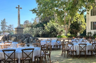 Tables élégamment dressées avec nappes blanches, serviettes pliées, verres et décorations florales dans une salle lumineuse.