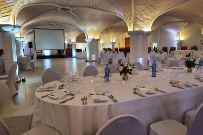 Salle de réception décorée avec des tables rondes, nappes blanches, rubans rouges et tonneaux en arrière-plan.