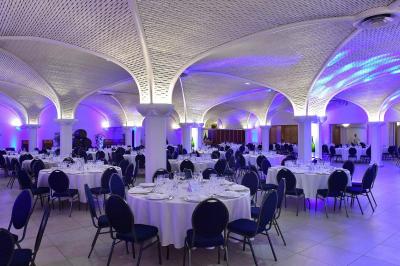 Salle de réception décorée avec des tables rondes, nappes blanches, rubans rouges et tonneaux en arrière-plan.