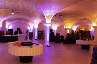 Salle de réception décorée avec des tables rondes, nappes blanches, rubans rouges et tonneaux en arrière-plan.