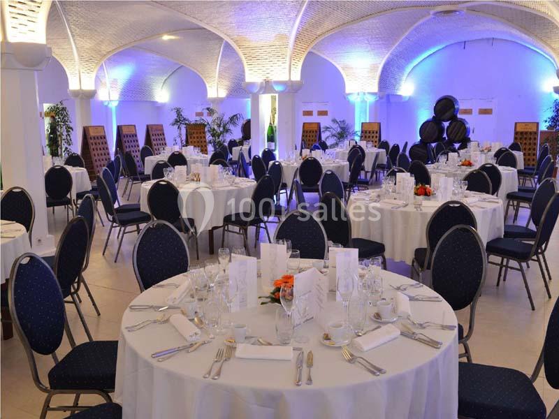 Salle de réception décorée avec des tables rondes dressées, chaises noires et éclairage d'ambiance bleu.