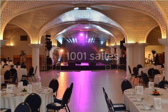 Salle de réception avec tables dressées et scène équipée de lumières et instruments de musique.