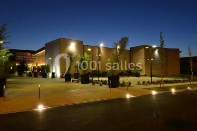 Salle de réception décorée avec des tables rondes, nappes blanches, rubans rouges et tonneaux en arrière-plan.