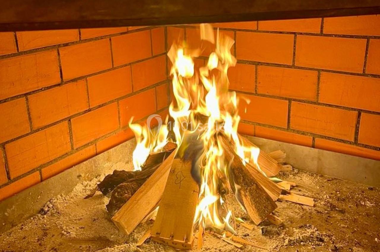 Feu de bois allumé dans une cheminée en briques orange, avec des flammes vives et des cendres au sol.
