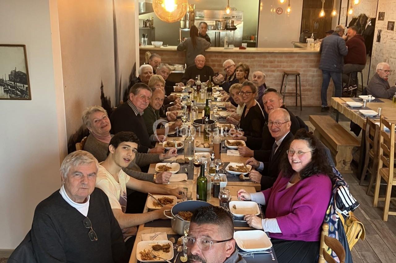 Un grand groupe de personnes partage un repas autour d'une longue table dans un restaurant chaleureux.