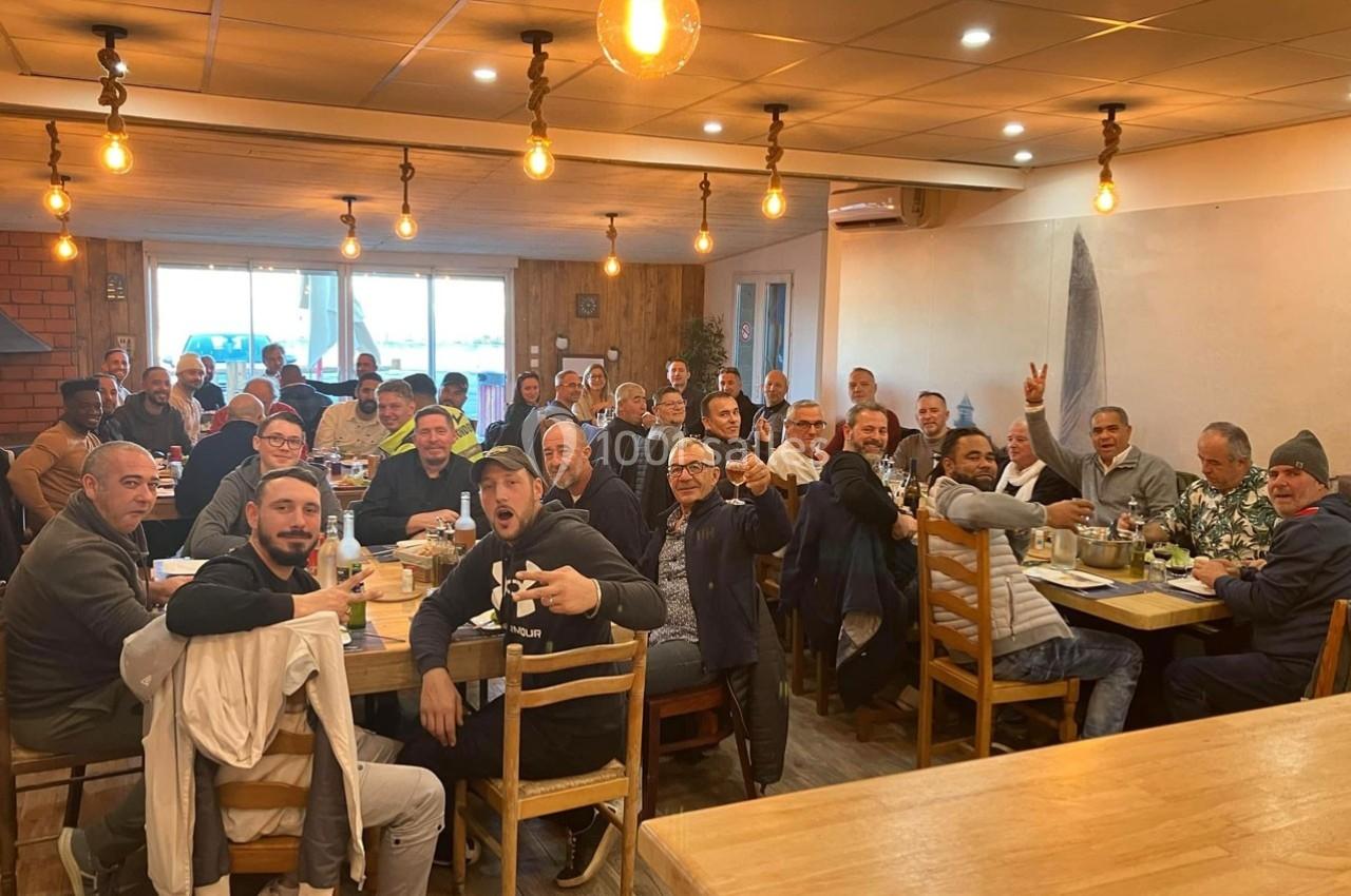 Un grand groupe de personnes assises autour de tables dans un restaurant, partageant un repas dans une ambiance conviviale.
