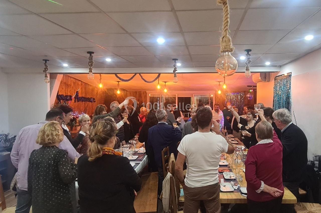 Des personnes réunies dans une salle décorée, levant leurs verres autour de tables dressées pour un repas festif.