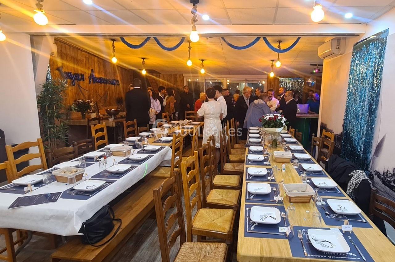 Salle de réception décorée avec des tables dressées et des invités debout en arrière-plan.