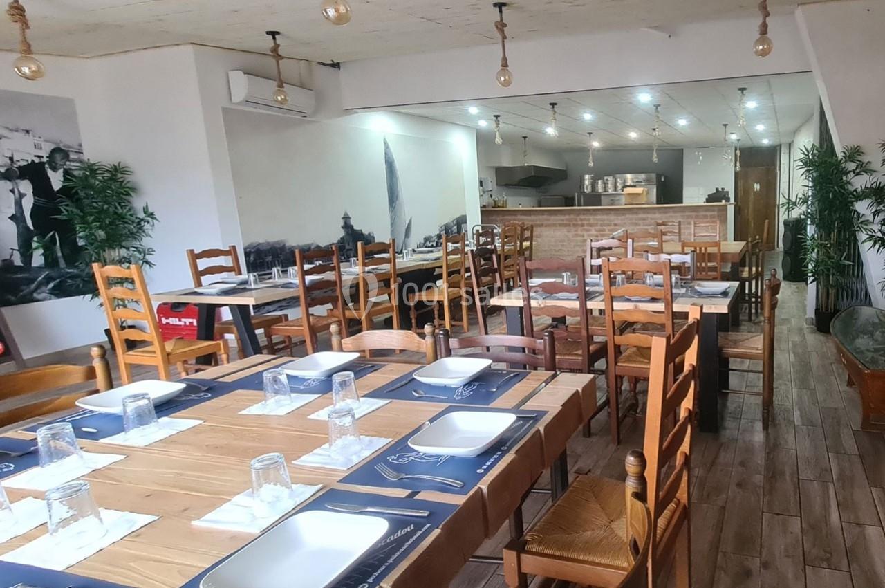 Salle de restaurant avec tables en bois dressées, chaises assorties et éclairage suspendu dans un décor sobre.