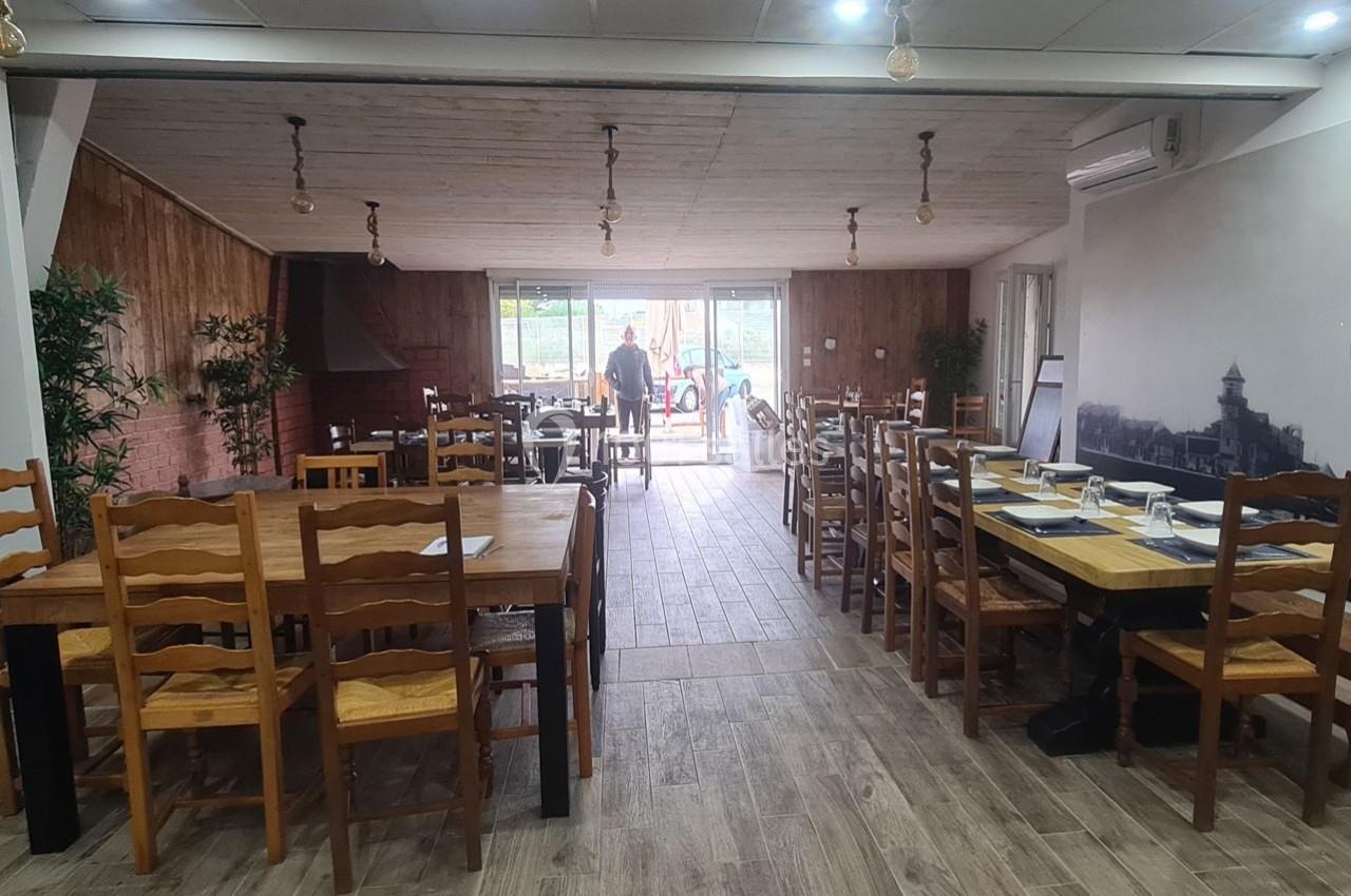 Salle de restaurant lumineuse avec tables en bois dressées, décor rustique et vue sur l'extérieur par une baie vitrée.