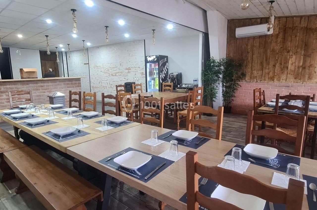 Salle de restaurant avec tables dressées, chaises en bois, murs en briques et éclairage suspendu.
