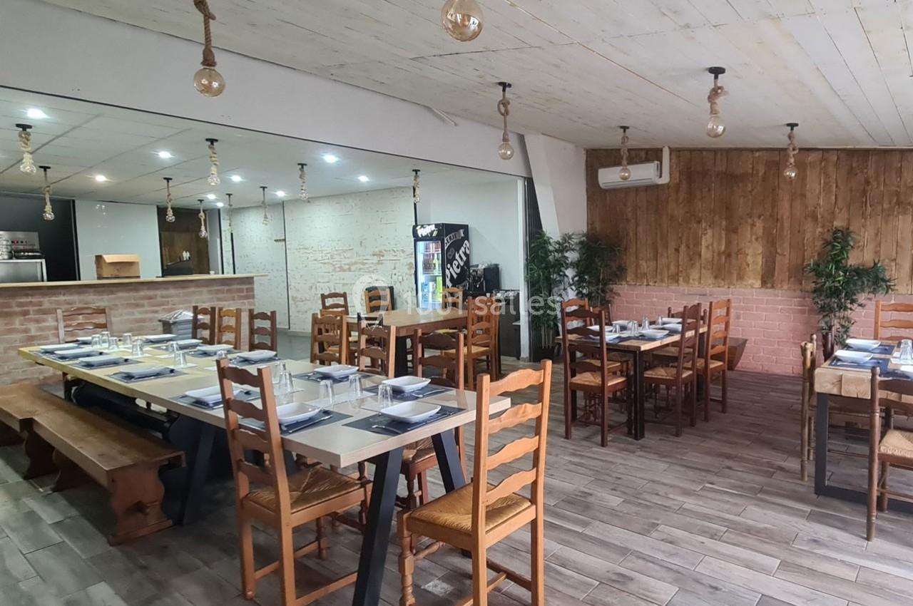 Salle de restaurant avec tables en bois dressées, éclairage suspendu et décorations murales en briques et bois.