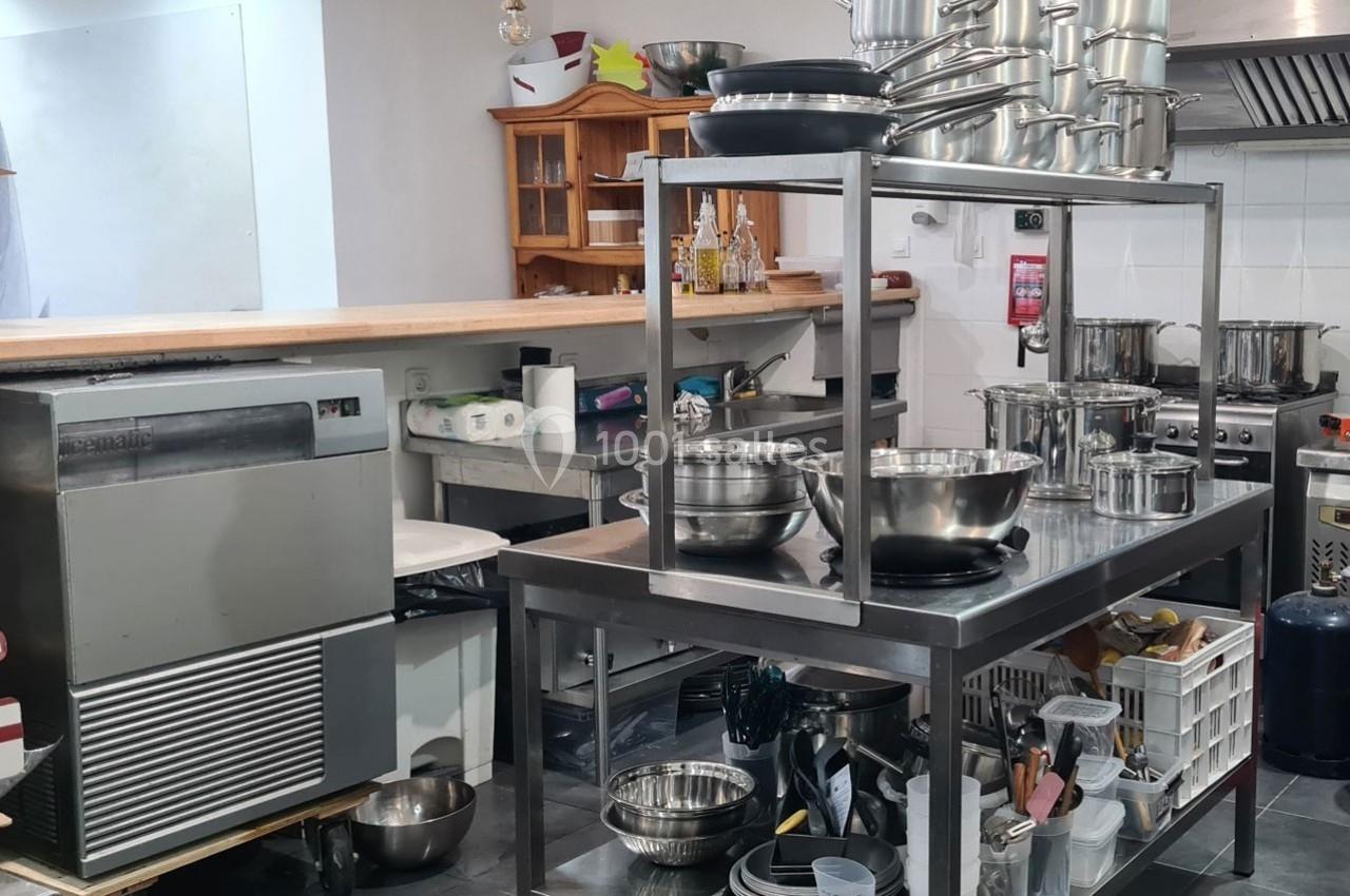 Cuisine professionnelle équipée avec plans de travail en inox, ustensiles, casseroles et appareils électroménagers.