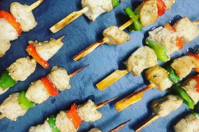 Deux hommes cuisinent des aliments sur un grand barbecue en plein air, éclairé par les flammes, à la tombée de la nuit.