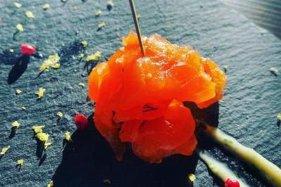 Deux hommes cuisinent des aliments sur un grand barbecue en plein air, éclairé par les flammes, à la tombée de la nuit.