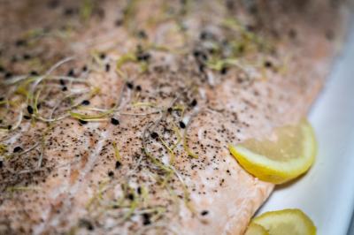 Deux hommes cuisinent des aliments sur un grand barbecue en plein air, éclairé par les flammes, à la tombée de la nuit.