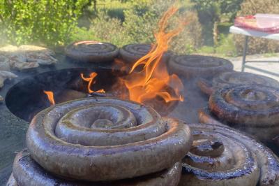 Deux hommes cuisinent des aliments sur un grand barbecue en plein air, éclairé par les flammes, à la tombée de la nuit.
