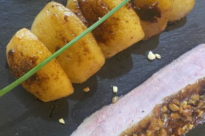 Deux hommes cuisinent des aliments sur un grand barbecue en plein air, éclairé par les flammes, à la tombée de la nuit.