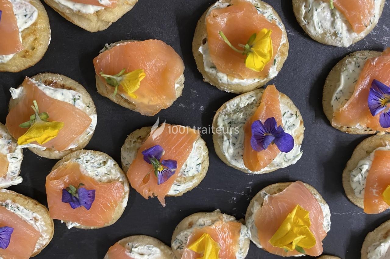 Canapés au saumon fumé garnis de fleurs comestibles et de fromage frais aux herbes, disposés sur une ardoise.
