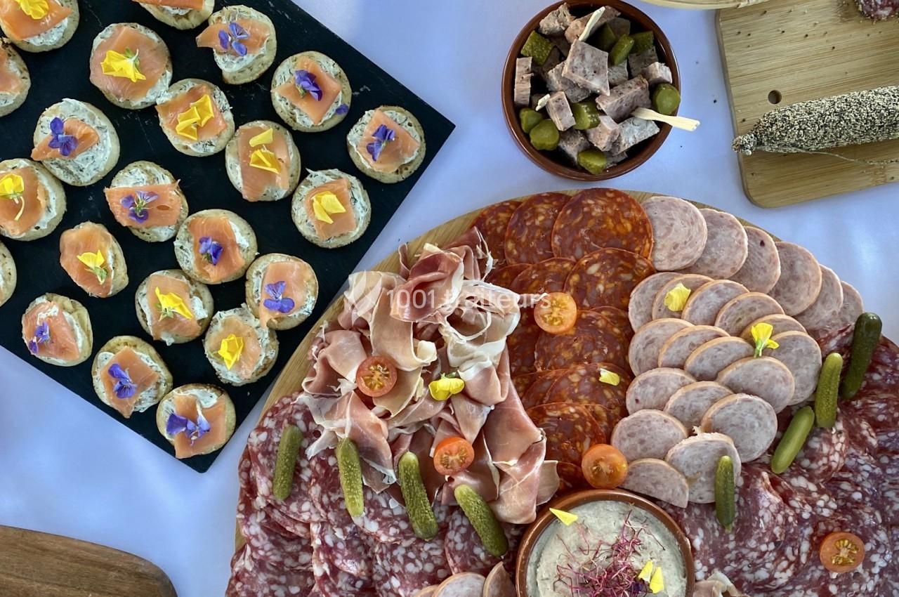 Plateau de charcuterie variée avec saucissons, jambon, cornichons, canapés au saumon et condiments sur une table.