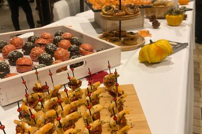 Deux hommes cuisinent des aliments sur un grand barbecue en plein air, éclairé par les flammes, à la tombée de la nuit.