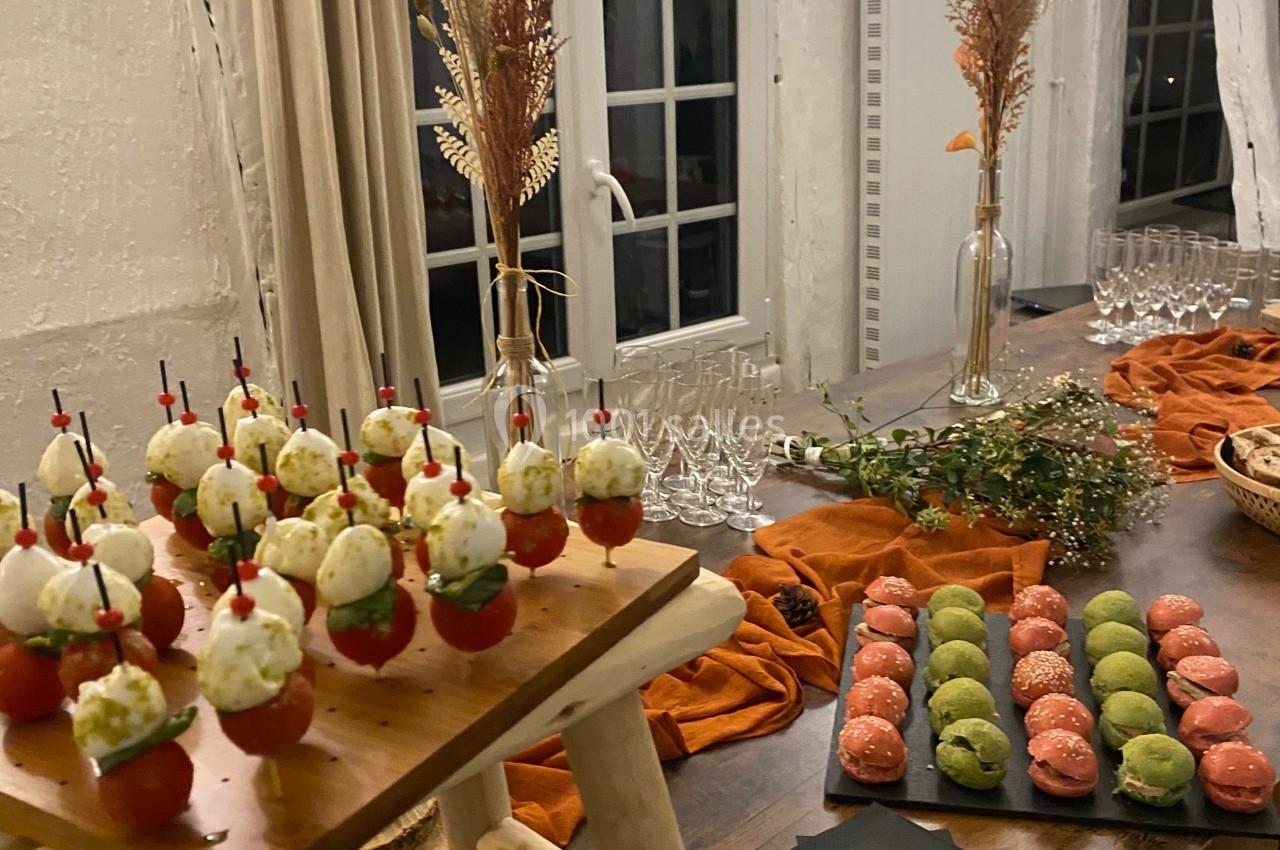 Buffet décoré avec des verrines, macarons colorés et éléments végétaux sur une table en bois dans une salle éclairée.