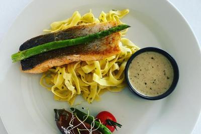 Deux hommes cuisinent des aliments sur un grand barbecue en plein air, éclairé par les flammes, à la tombée de la nuit.