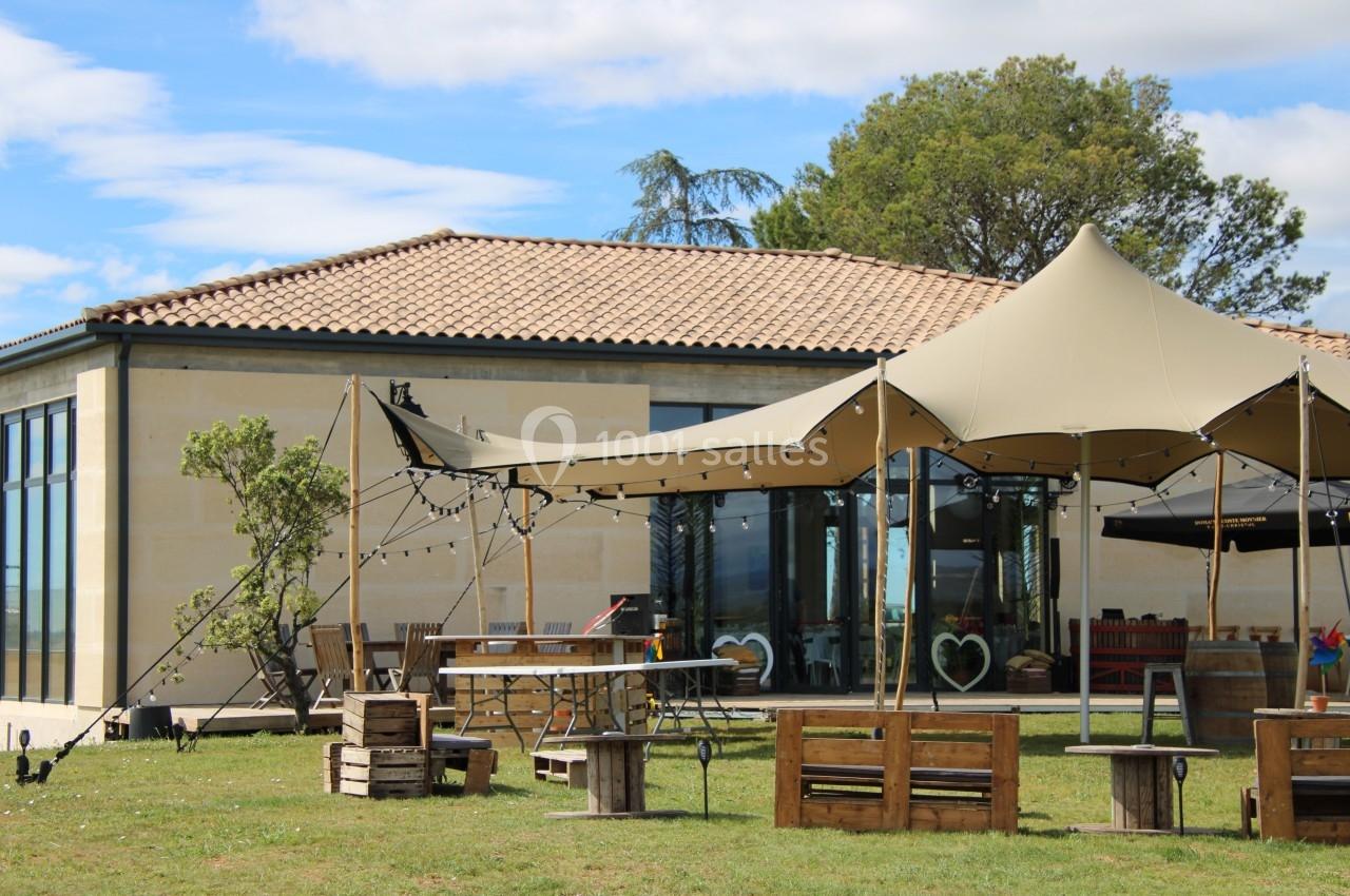 Tente beige installée devant un bâtiment en pierre avec des tables, des bancs et des décorations en extérieur.